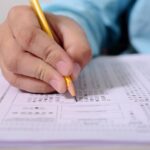 Person writing on paper with pencil.