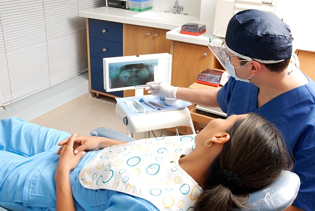 Woman in dental chair with man in background.