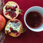 A pomegranate and a cup of tea placed on a red table.