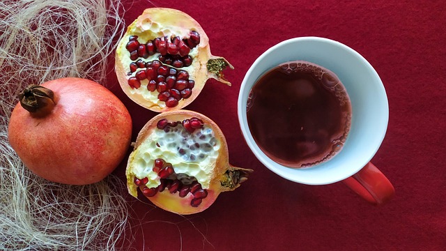 A pomegranate and a cup of tea placed on a red table.