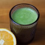 Healthy green drink and a ripe orange placed together.