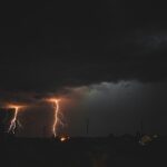 Lightning strikes over dark sky with distant light.