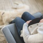 A pregnant woman sitting on a couch with her dog.